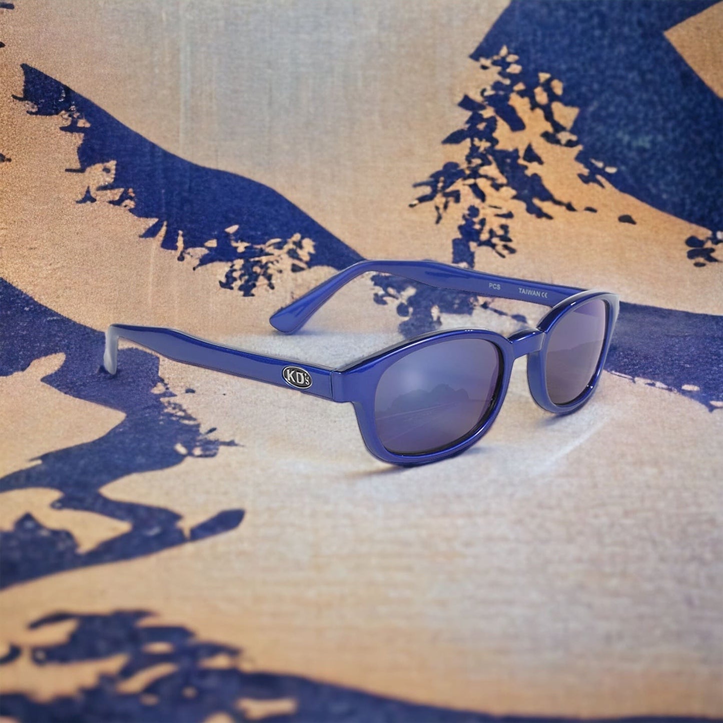KD's 20122 sunglasses that fit under a motorcycle or ski helmet. For bikers and sportsmen. With a blue metallic frame and blue mirror lenses in front of a decorated canvas.