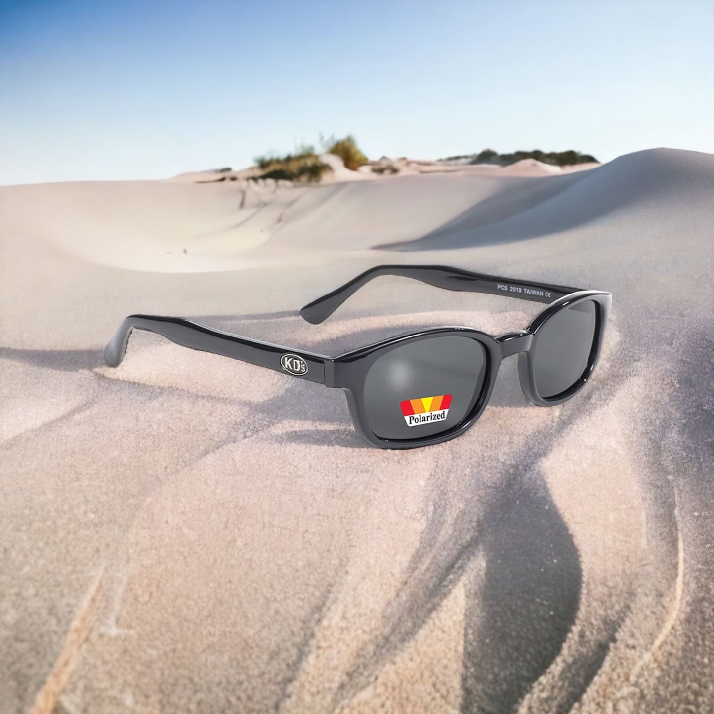 The KD's 2019 sunglasses ideal for outdoor activities with grey polarized lenses laid on the sand in the desert.