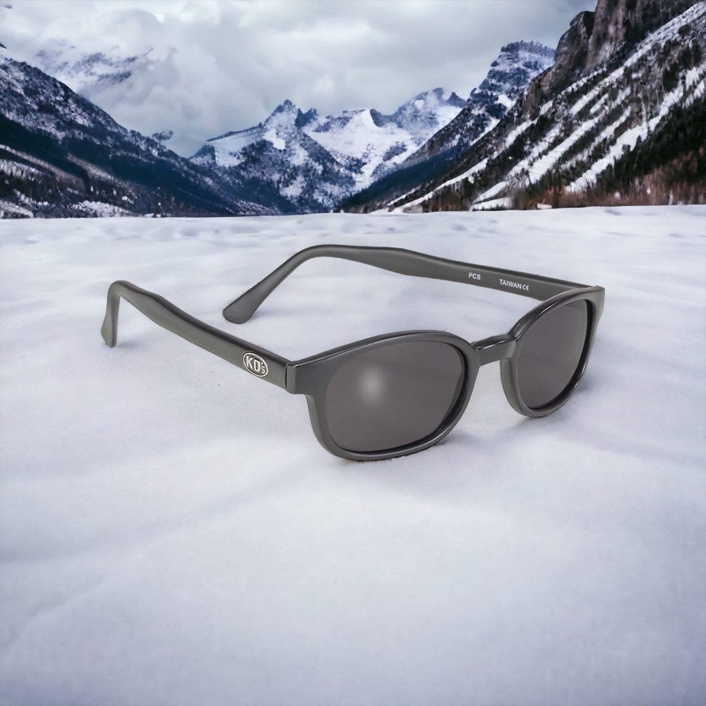 KD's 21120 sunglasses that fit under a motorcycle or ski helmet. Worn by SAMCRO bikers and Jax Teller in Sons of Anarchy. With a sleek matte black frame and smoked lenses. Posed in the snow in the mountains.