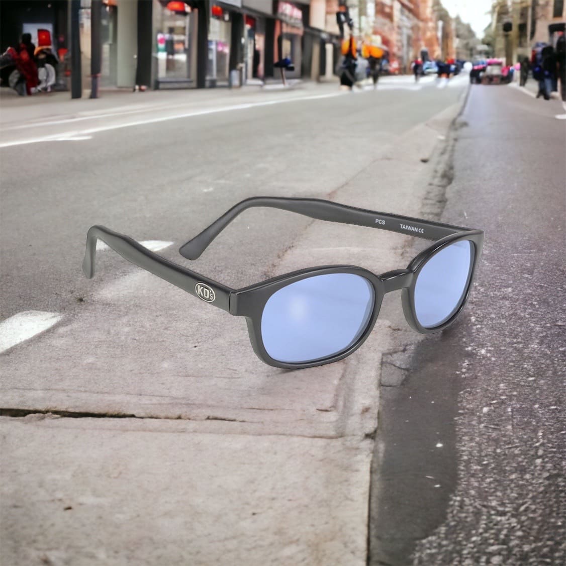 KD's 20012 sunglasses that fit under a motorcycle or ski helmet. With a durable matte black frame and blue tinted polycarbonate lenses set on the road in the street.