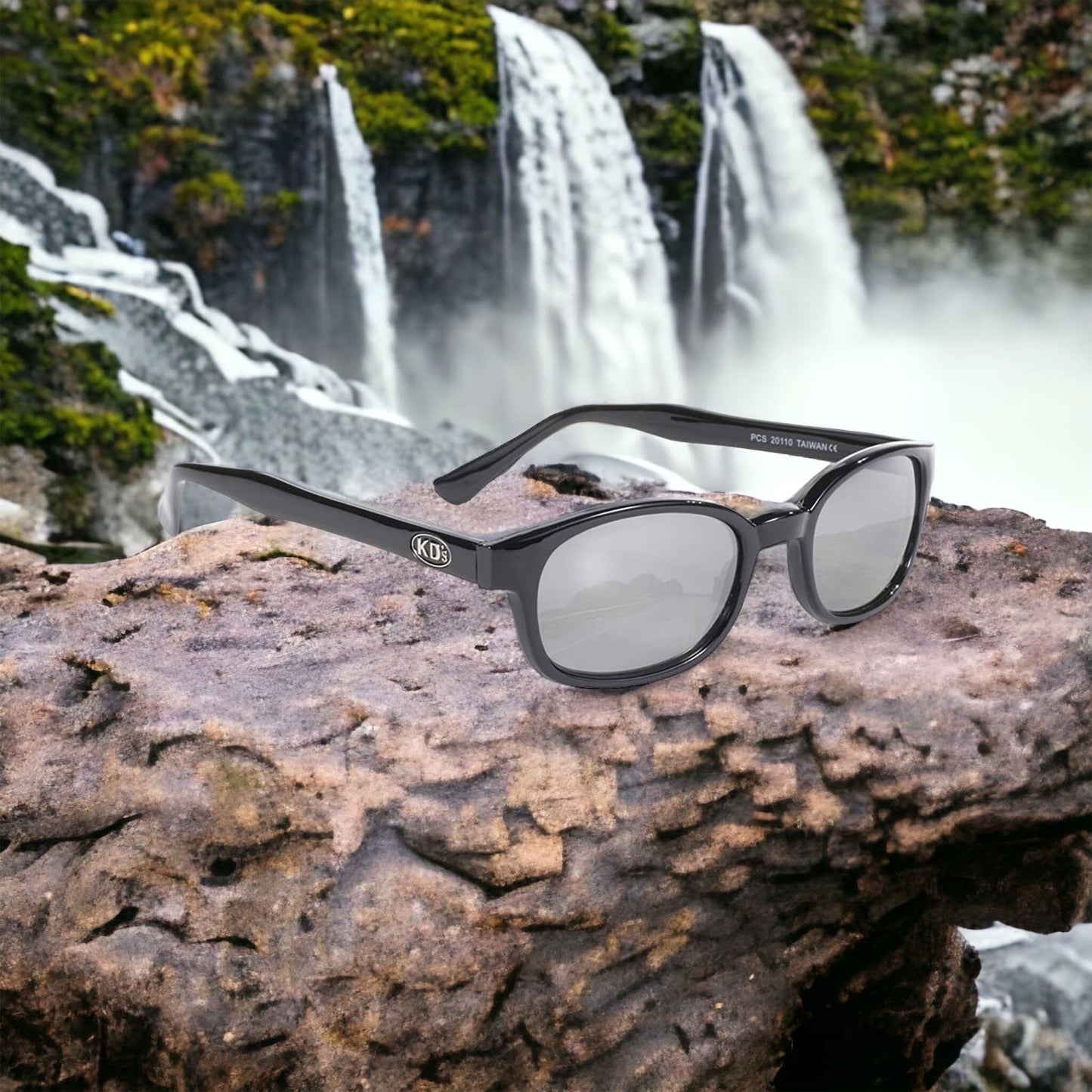 KD's 20110 sunglasses that fit under a motorcycle or ski helmet. With a stylish black frame and silver mirror lenses set on a rock in front of a waterfall.