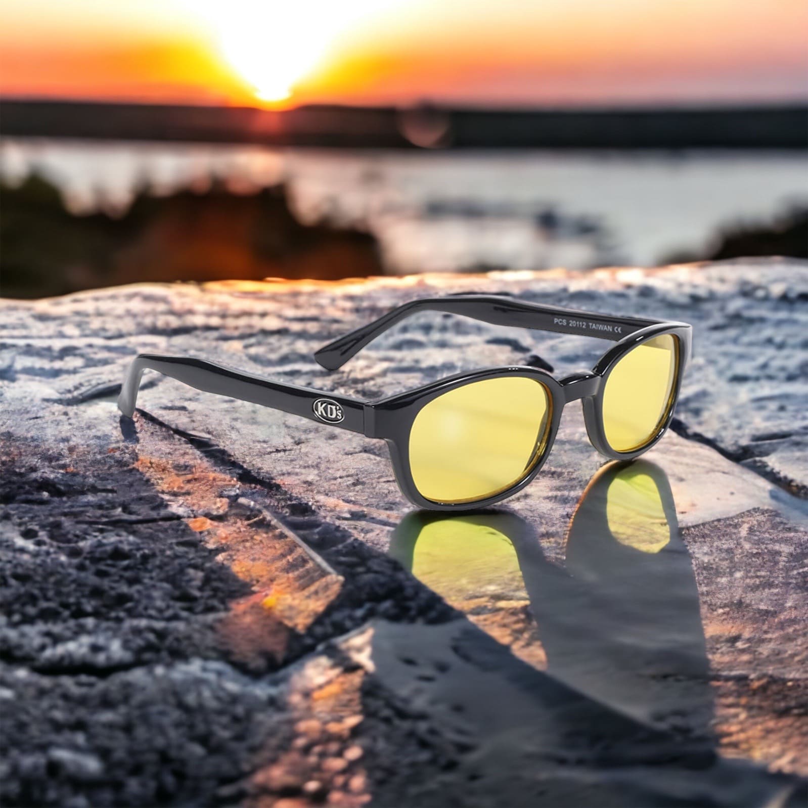 KD's 20112 sunglasses that fit under a motorcycle or ski helmet. With a stylish black frame and yellow tinted lenses set on a cliff in front of a sunset.