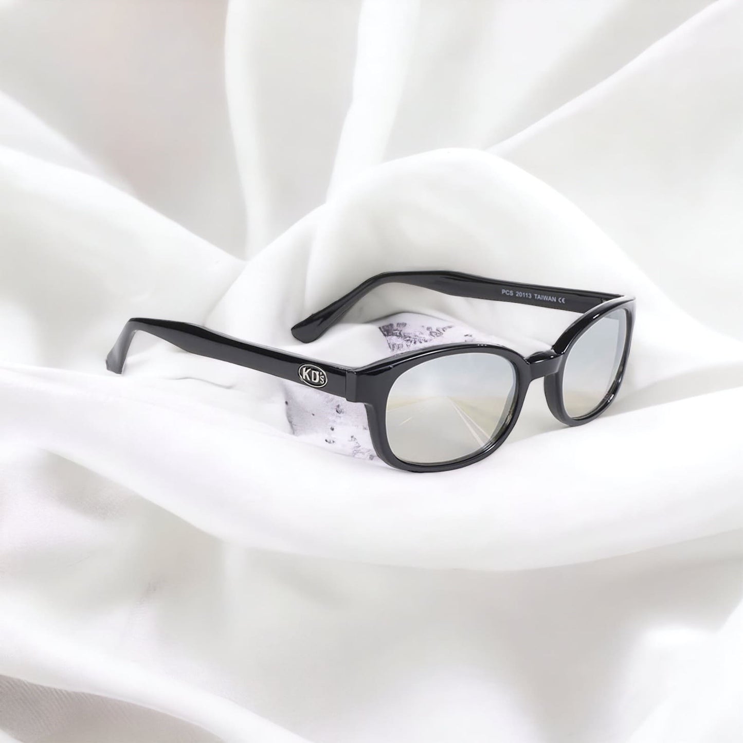 KD's 20113 sunglasses that fit under a motorcycle or ski helmet. With a classic black frame and clear silver mirror lenses set on a white silk sheet.