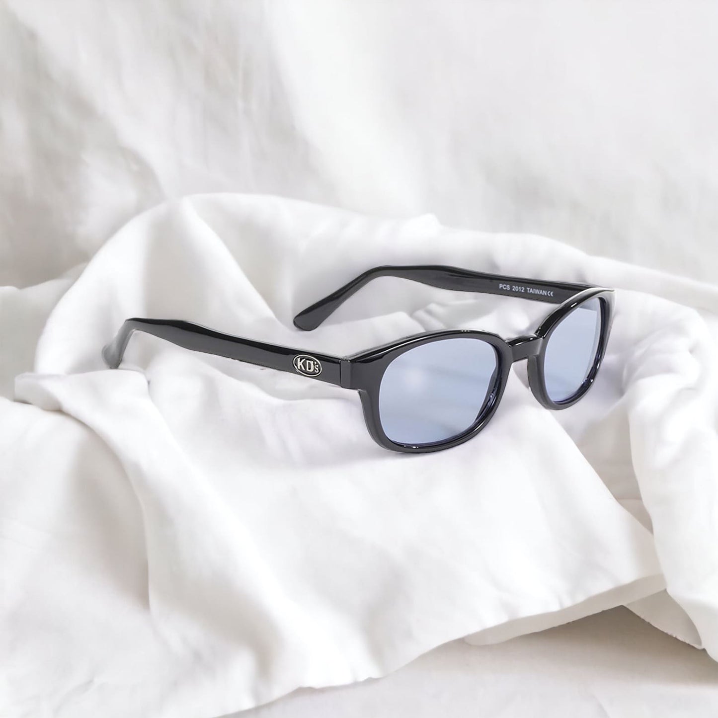 The sunglasses KD's 2012 that fit under a ski or motorcycle helmet with light blue lenses laid on a bed with white fabric.