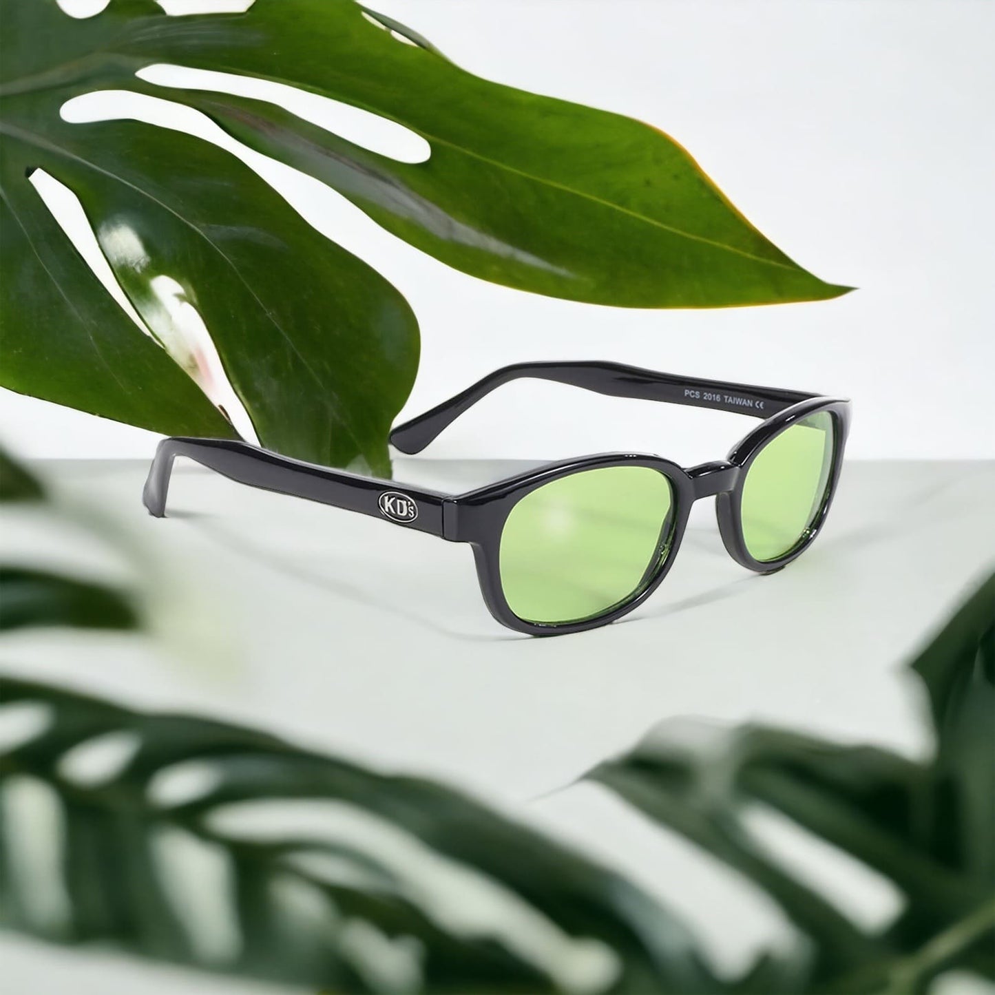 The KD's 2016 sunglasses that fit under a helmet for outdoor activities with light green lenses placed on a white table surrounded by plants.
