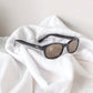 The KD's 2121 sunglasses worn by SAMCRO bikers in the Sons of Anarchy series with brown lenses and a resistant black frame placed on white bed linen.