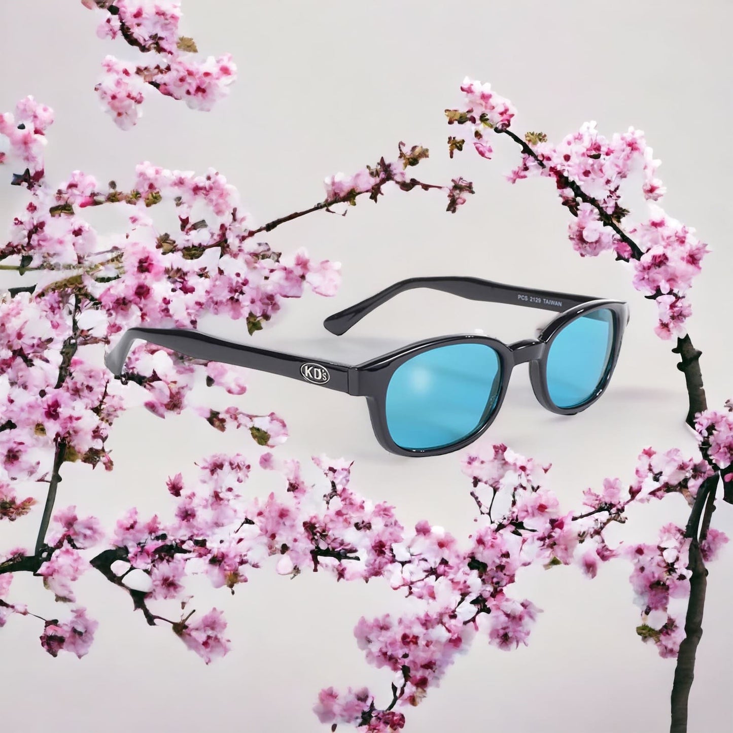 The stylish KD's 2129 sunglasses with turquoise blue polycarbonate lenses and a solid black frame set on cherry blossoms.