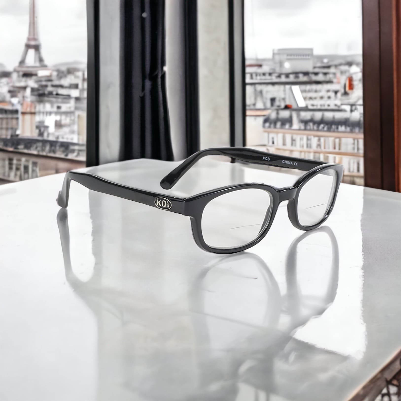 KD's readerz sunglasses with correction index. Worn by Jax Teller in Sons of Anarchy. With a stylish black frame and clear lenses. Placed on a table in front of a window with a view on Paris.