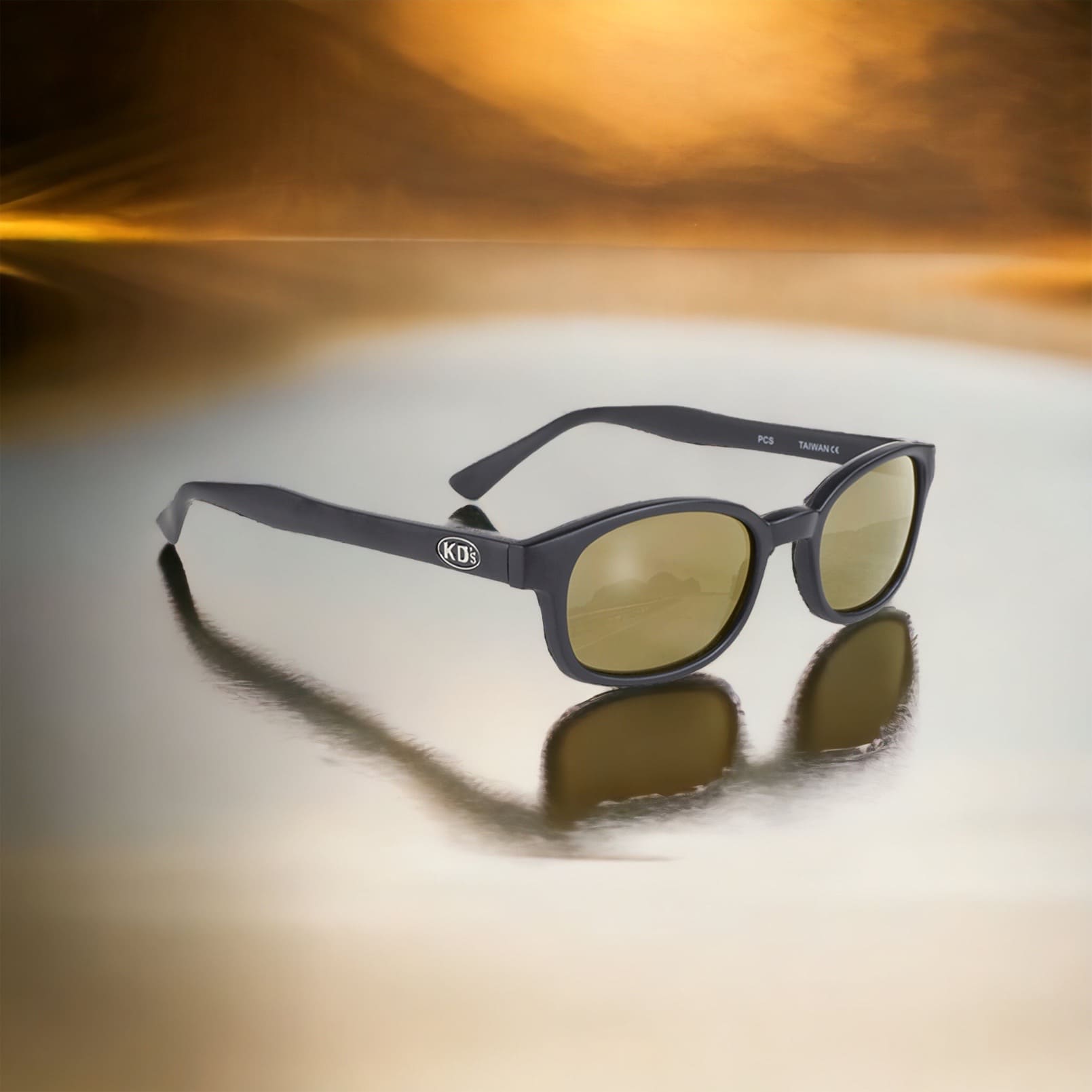 X-KD's 1000 Sunglasses with a matte black frame and golden mirror lenses set on a shiny surface