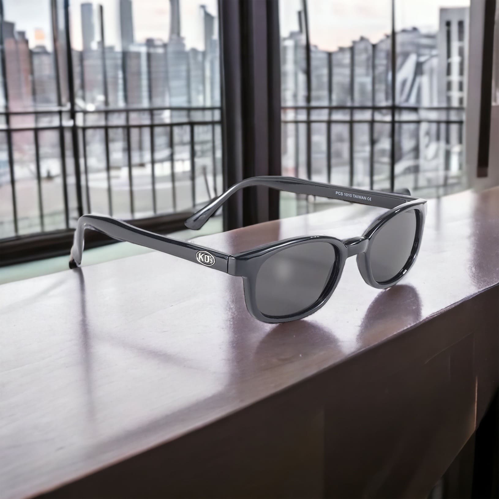 The X-KD's 1010 sunglasses worn by Jax Teller in Sons of Anarchy with an elegant black frame and smoked lenses. Placed on a window with a view of New York