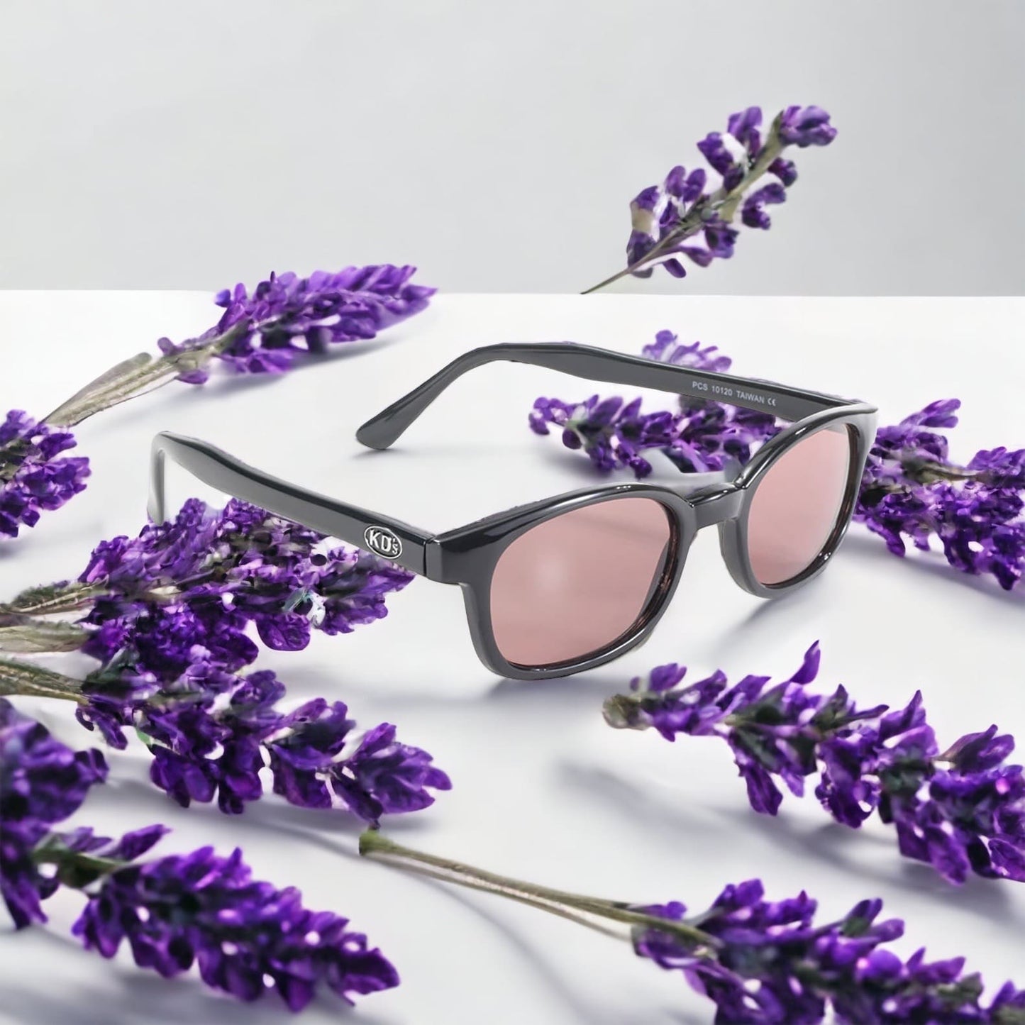 X-KD's 10120 large sunglasses for sportsmen and bikers with a refined black frame and pink tinted polycarbonate lenses on a lavender bed.
