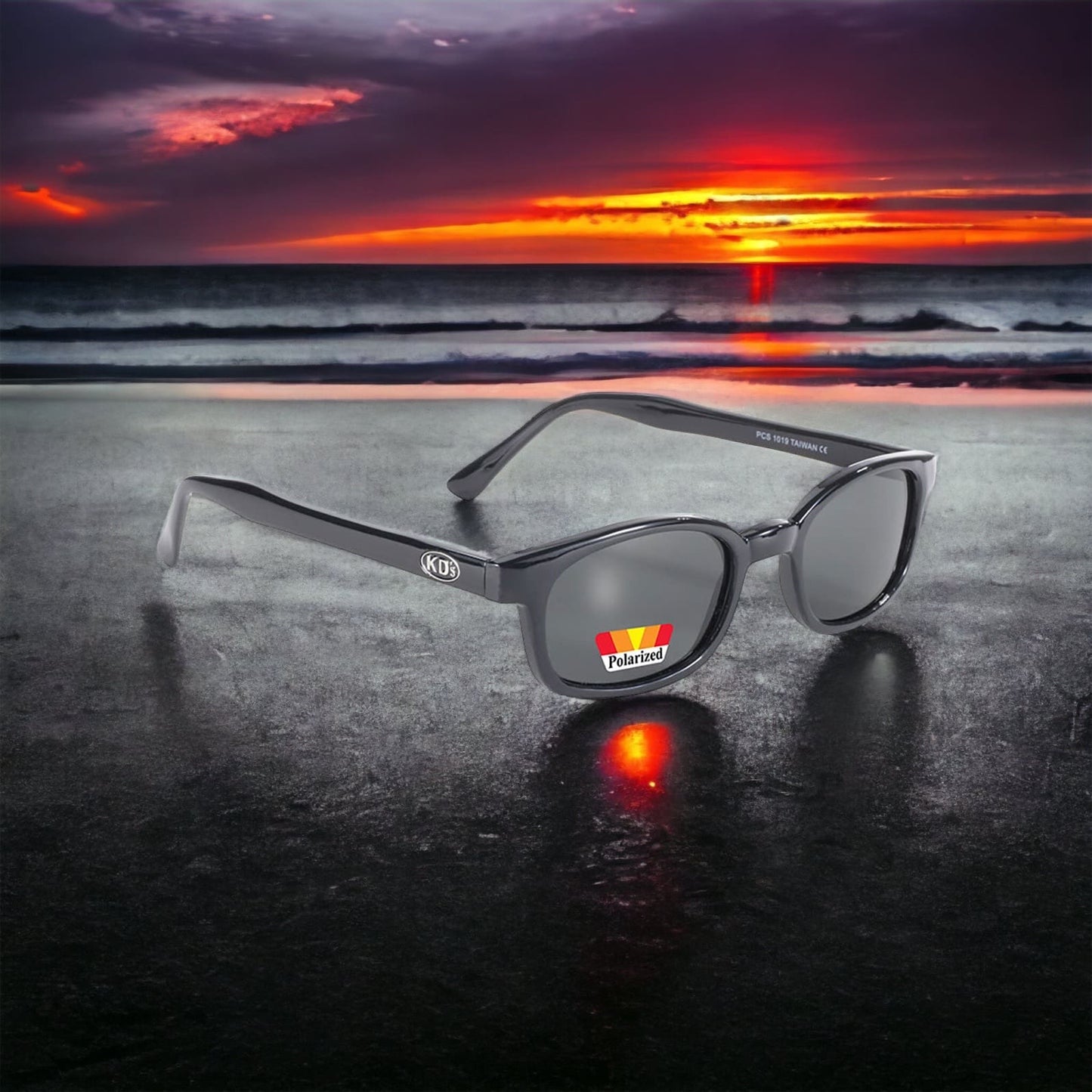 The X-KD's 1019 sunglasses with polarized grey lenses and a chic black frame placed on the beach behind a sunset