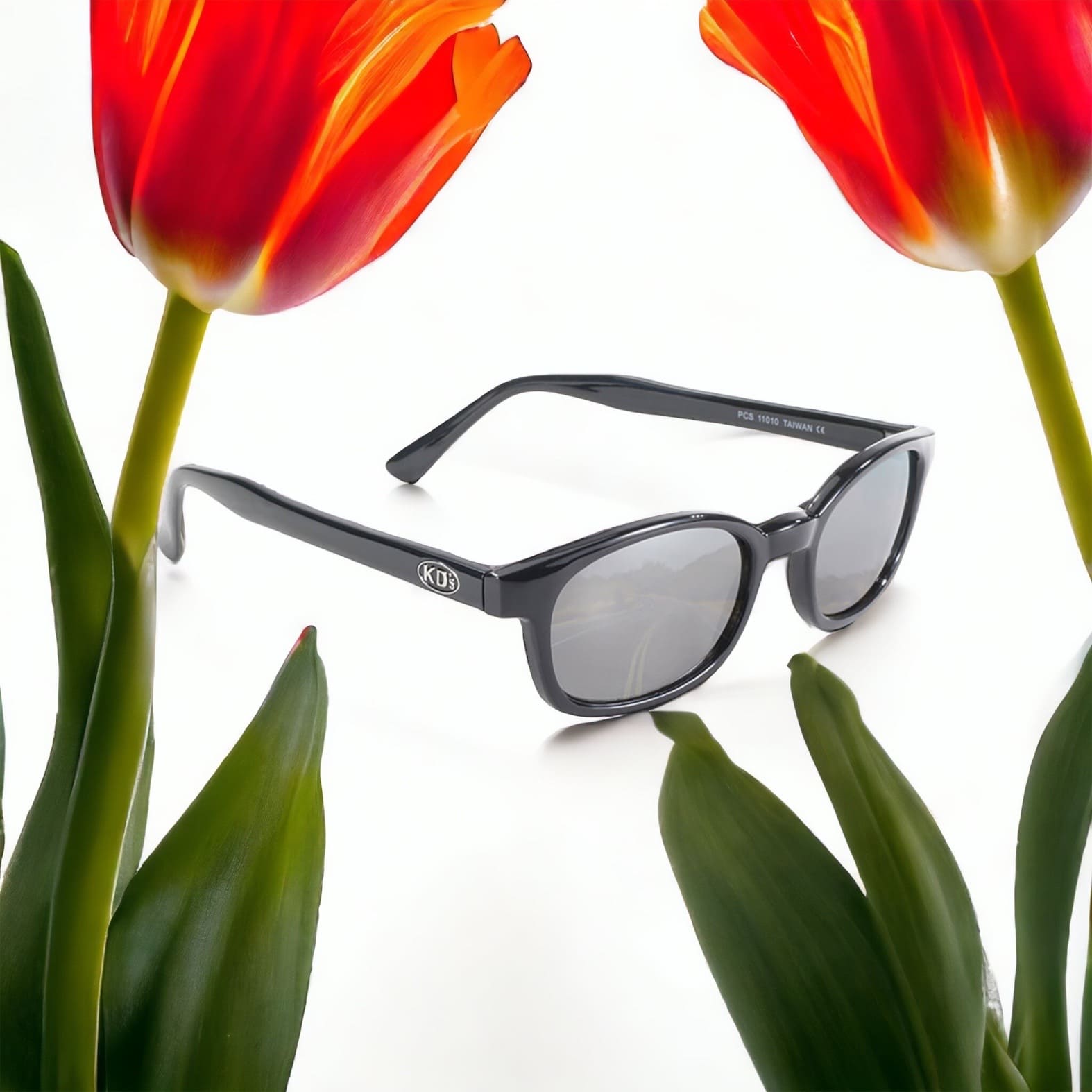 X-KD's 11010 large sunglasses for outdoor activities with a sleek, rugged black frame and silver polycarbonate mirror lenses set in front of tulips.