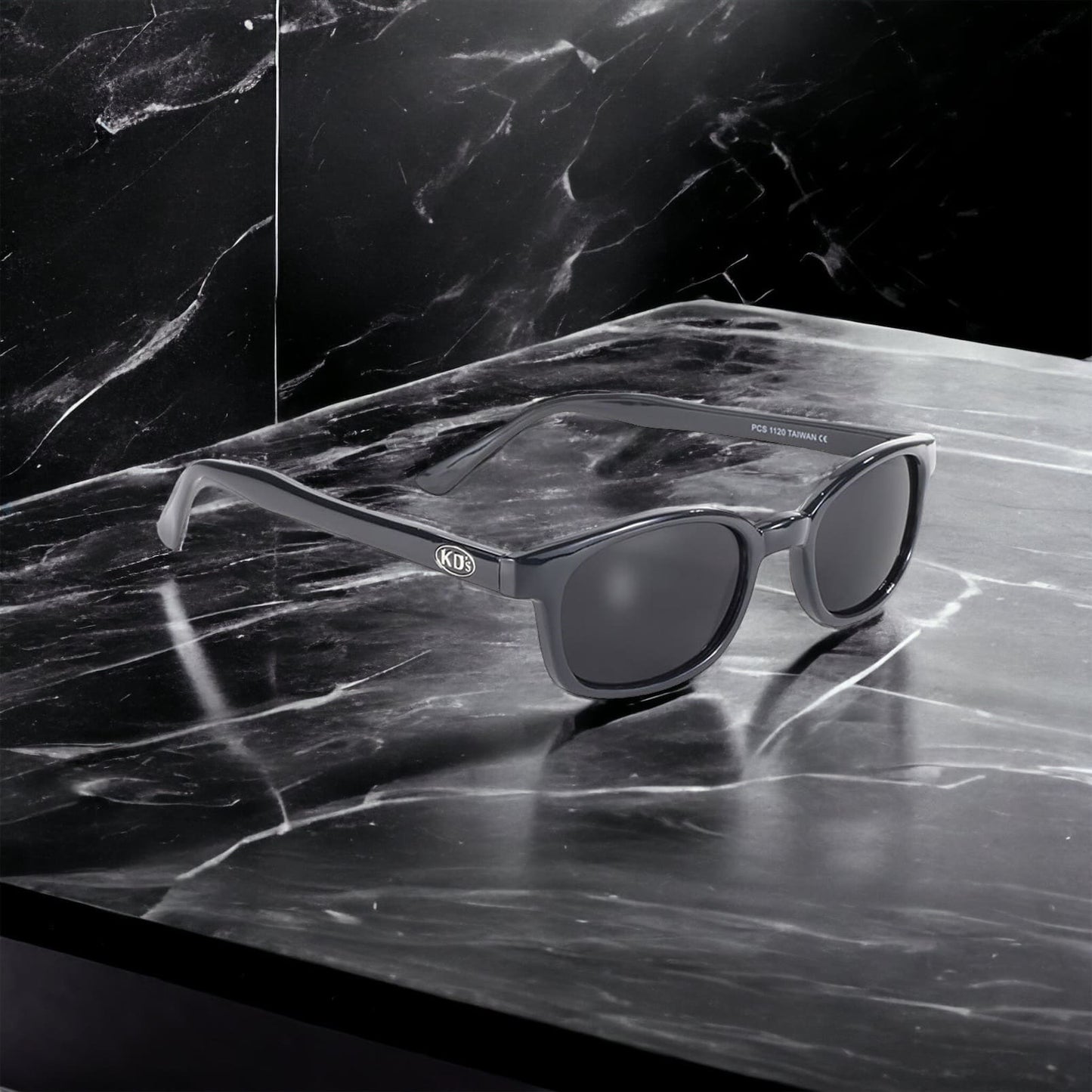 X-KD's 1120 sunglasses with dark grey lenses and a refined black frame placed on a black marble countertop.