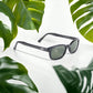 The X-KD's 1126 sunglasses with dark green lenses and a harmonious black frame placed on a white table surrounded by leaves.