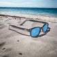 The X-KD's 1129 sunglasses with turquoise lenses and a classic black frame placed on the sand at the beach.